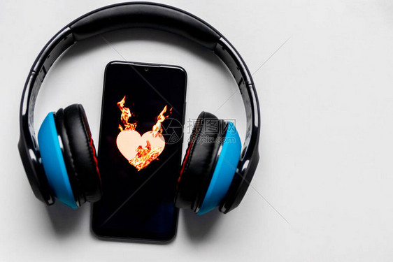 黑色智能手机屏幕上燃烧着火焰的燃烧心脏符号和耳机和复制空间上的蓝色显示了对音乐和移动收听音乐和音乐流媒图片