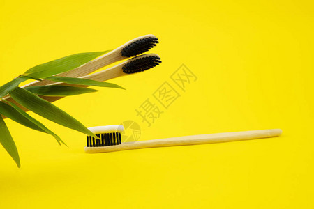 黄色背景上有天然刷毛和牙膏的竹制天然牙刷带竹叶的木制牙刷零浪费爱护环图片