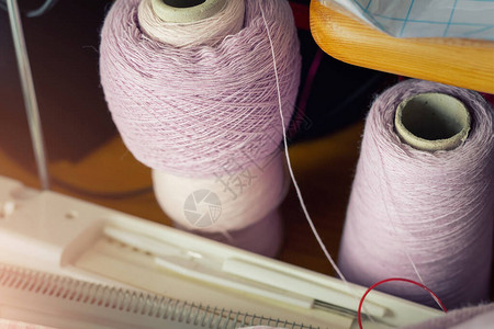 桌上有粉紫色羊绒丝毛线的两个纸筒和针织机零件设备DIY手工爱好工艺背景图片