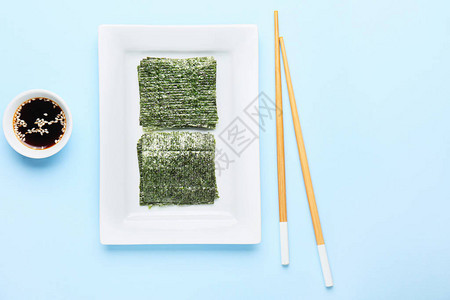 彩色背景上带有美味海藻片酱油和筷子的盘子图片