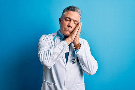 穿着大衣和蓝色听诊器的中年长英俊灰发医生男子睡着疲倦的梦境图片