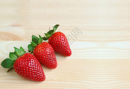 木质桌上三个亮红色新鲜的里普草莓水果图片
