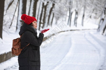 穿着冬大衣的年轻美丽微笑的女子在城市森林公园下雪天气图片