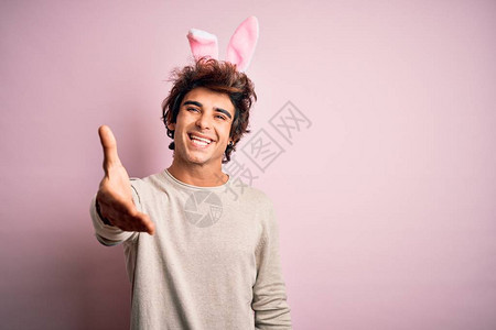 英俊的年轻人拿着复活节兔子耳朵站在孤立的粉红色背景上图片