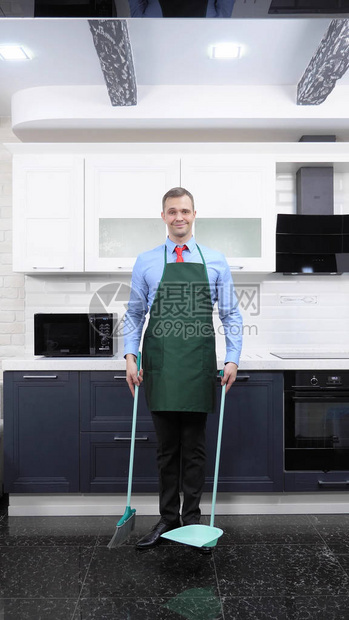 打着领带和围裙的英俊男人正在扫厨房的地板图片
