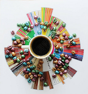 在品尝者的风味轮上的白杯黑咖啡多色珍珠彩绘咖啡豆四处散落顶视图第三波背景图片