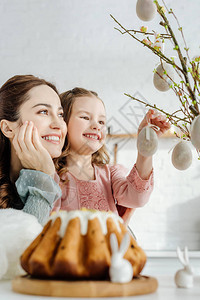 快乐的母女选择地看着装饰着复活节彩蛋的柳枝图片
