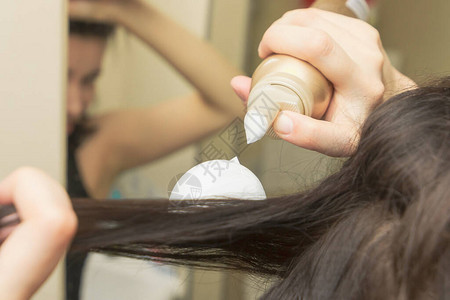年轻女用泡沫或慕斯塑头发在棕色长直图片