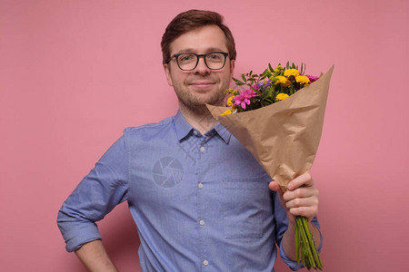 蓝衬衫和眼镜的年轻caucasian男子拿着鲜花作为生日礼物送给母亲或女朋友纪念日的概念工作室在图片