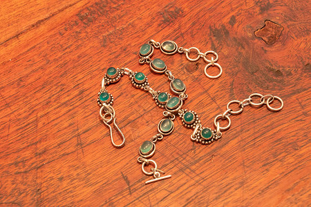 银色的两只绿洋葱珠链手镯在木桌背景图片