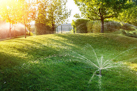 在草坪下安装不同喷头的景观自动花园浇水系统日落时使用智能自动喷雾器灌溉草坪山丘和果图片