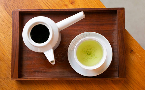 白杯中的日本绿色茶叶和黑木制的茶壶图片
