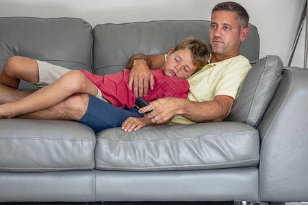 一个睡着的年轻男孩躺在沙发上和他爸一起看电视他们图片
