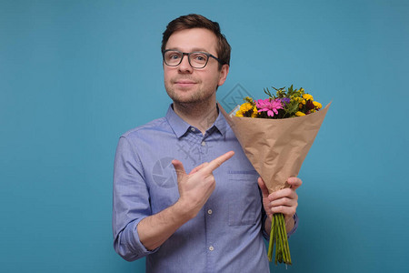身穿粉色t恤的年轻白人男子拿着鲜花作为生日礼物送给母亲或女朋友周年纪念礼物的概念在彩色墙上图片