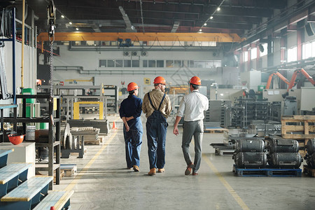 三名年轻当代工人的后视力在大型工厂和通信中行走的工业图片