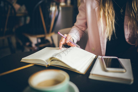 商业教育理念在咖啡店户外工作的女人在咖啡馆内的木桌上特写白种女人的手在笔记本上做笔记在笔记图片
