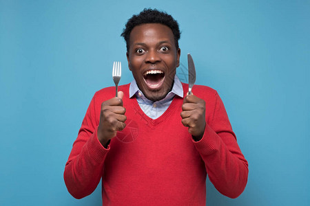 饥饿的非洲青年男子拿着叉子和刀等美味的饭菜图片