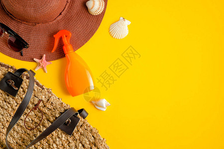 黄色背景的橙色塑料瓶太阳镜沙滩帽和藤袋中的防晒喷雾乳液图片