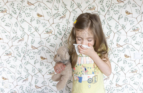 一个学龄前的小女孩因为感冒而在餐巾纸上打喷嚏图片