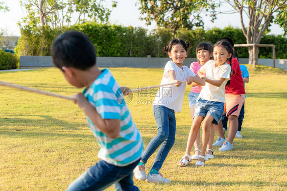 一群快乐的亚裔儿童在夏季天到城区公园操场玩拖战或拉绳牵引器图片