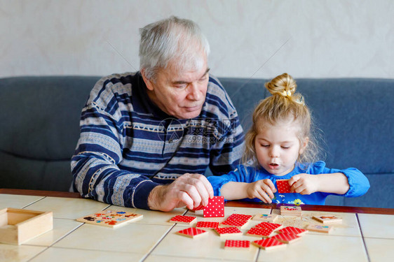 美丽的蹒跚学步的女孩和祖父在家里一起玩图片记忆桌牌游戏可爱的孩子和老人一起玩乐室图片