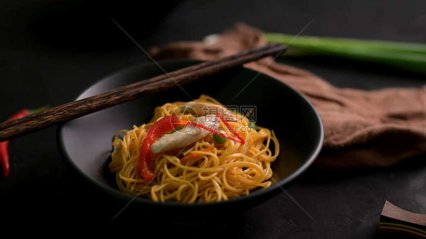 在黑碗中用筷子在黑桌上割成的Schezwan面条或Cho图片