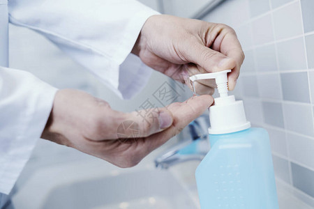 身穿白色大衣的天主教医生用从蓝色瓶子中洗手剂为图片