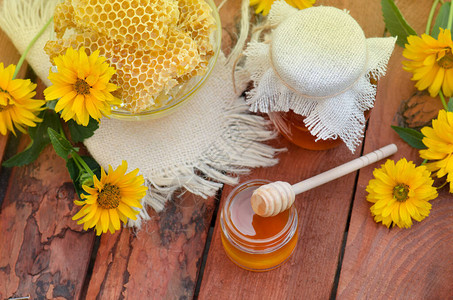 蜂蜜的罐子有鲜花背景的木桌上的蜜蜂窝图片