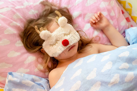 小女孩戴着有趣的鹿形毛绒面具安静地睡在床上就寝时间孩子睡在有云的床单上背景图片
