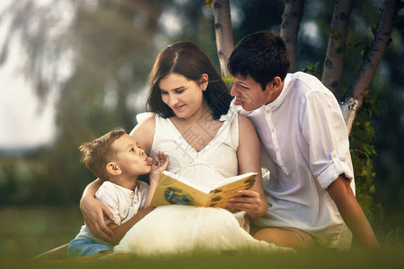 快乐的年轻家庭在一棵树下阅读本书图片