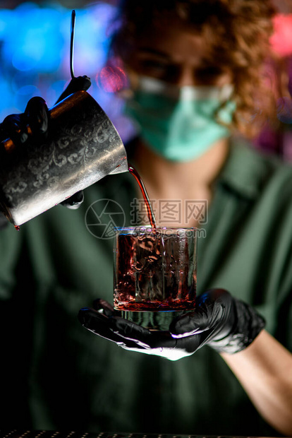 戴着医用口罩的女酒保一只手拿着玻璃图片