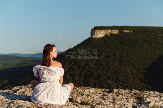 身着白色连衣裙的美丽年轻女子在日落时分在山上欣赏壮丽的景色概念设计成功的女徒步旅行者在日出山顶张开双臂一图片