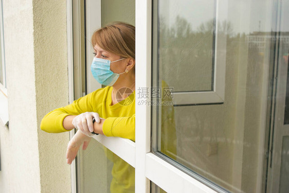 这名戴着防护口罩和手套的妇女站在公寓敞开的窗户前图片