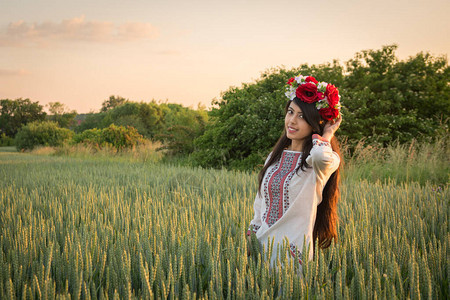 漂亮的年轻女子穿着传统的乌克兰服装和花环在麦田里散步图片