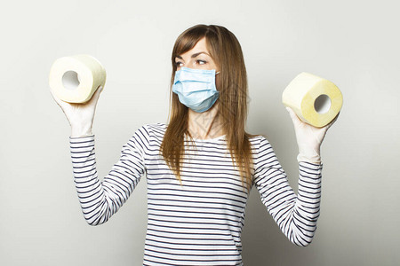 身戴医疗面具和手套的年轻女孩携带两卷卫生纸图片