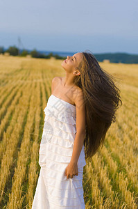 一个美丽的长发在风中飘扬的少女站在割草的麦田和湛蓝的图片