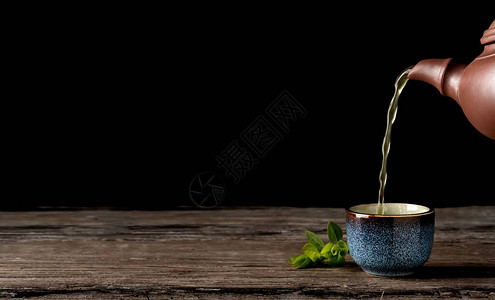 热绿茶从壶倒进蓝色碗里背景图片