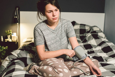 题目高血压高血压病22岁的年轻白种人妇女使用自动眼压计她把袖口放在胳膊上检查压力回家在卧室的床背景图片