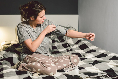 题目高血压高血压病22岁的年轻白种人妇女使用自动眼压计她把袖口放在胳膊上检查压力回家在卧室的床背景图片