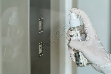 穿戴医疗手套将抗细菌防剂喷雾洒到电梯按钮上后再按下清洁机图片
