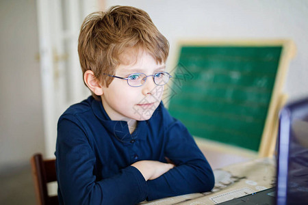 戴着眼镜在电脑上做学校作业的小学生儿童在pc上学习的男孩在隔离期间因电晕流行病而锻炼在图片