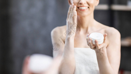 皮肤护理无法辨认的成熟女士在家里的浴室里拿着面霜保湿和护理皮肤全景图片