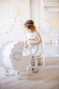 穿着白色连衣裙的可爱小女孩在明亮的儿童房里玩着一个白色的洋娃钉子图片