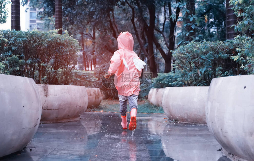 身穿粉红色雨靴和在水坑里跳水时行走图片