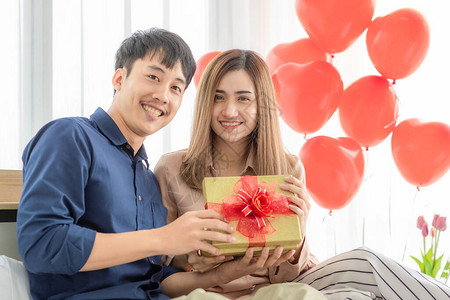 年轻而微笑的亚洲男人送礼和打开礼盒图片
