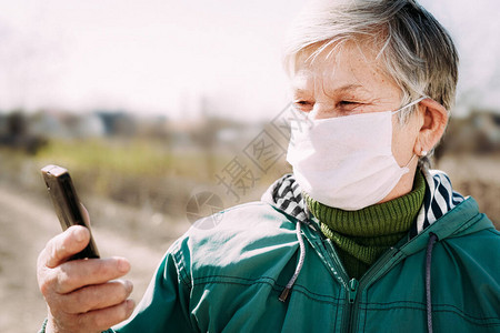 在电晕和流感爆发期间戴口罩的高级妇女用于老年人预防冠状的外科口罩用手机阅背景图片