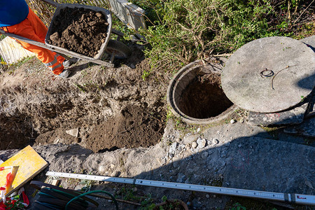 建筑工人推着装满重土的独轮车的高角度视图下水道井施工现场与地板上的公图片