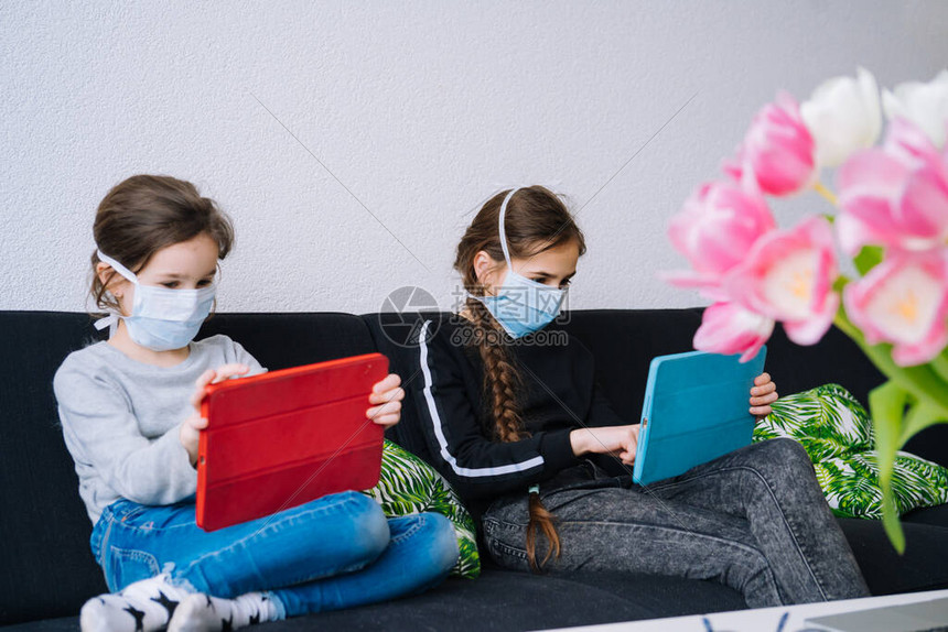 在线教育远程学习在家上学戴着医用口罩的孩子们在家上网课时用笔记本电脑的数字平板电脑学习作业隔离时的社会距图片