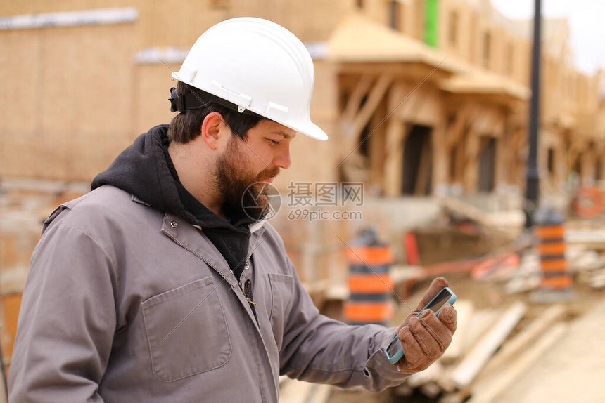 白种人建造者在建筑工地使用手机互联网并戴着安全帽建筑专业和房图片