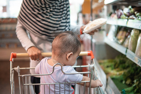 坐在购物车或杂货超市小货车上的母亲推着的婴图片